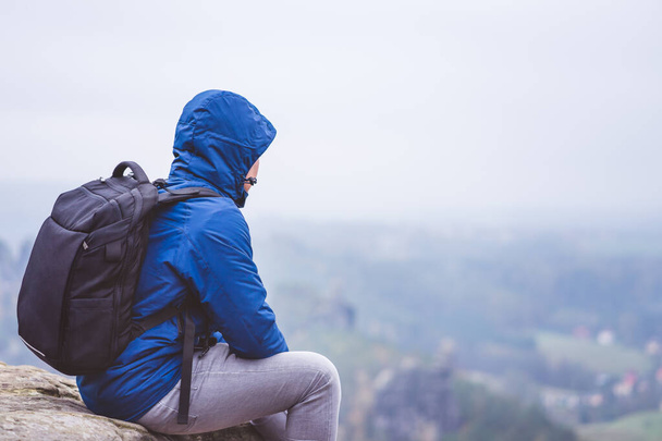 Lonely hiker wear outdoor clothing with backpack sitting on mountain edge, enjoying view of defocused valley. Travel adventure lifestyle harmony concept - Photo, Image