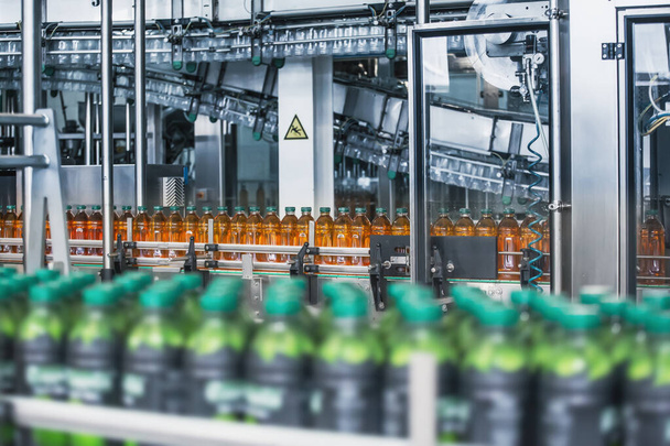Пластиковые бутылки со свежим органическим соком на автоматической конвейерной ленте или линии на заводе напитков или внутри завода с современным промышленным оборудованием
 - Фото, изображение