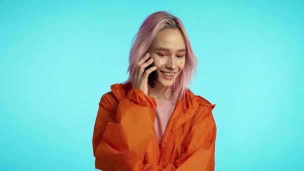 Smiling unusual hipster talking on mobile phone over blue background. Beautiful woman holding and using smart phone. Girl with technology - Filmmaterial, Video
