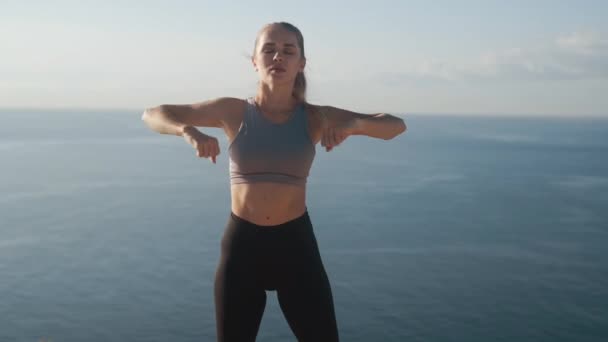 Woman does exercises and stretches at morning, sea on background, slow motion - Filmati, video