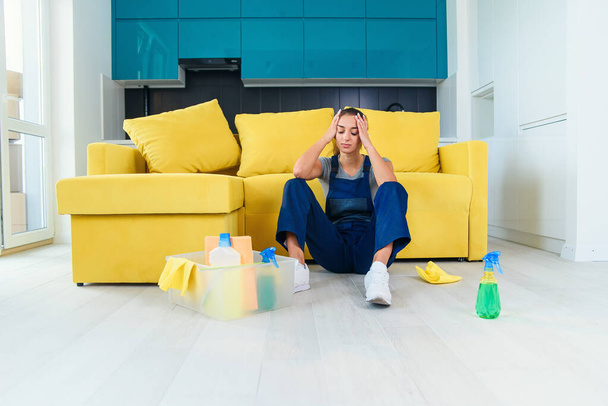 Young female worker of the cleaning service sitting near the couch and feeling tired after washing floor on cuisine. - Fotó, kép