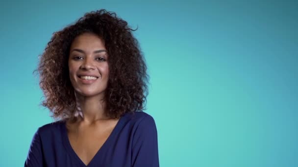 Copiar espacio. Mujer africana bonita con pelo afro en ropa de negocios sonriendo a la cámara sobre fondo de pared azul. Linda raza mixta niñas retrato
.  - Imágenes, Vídeo