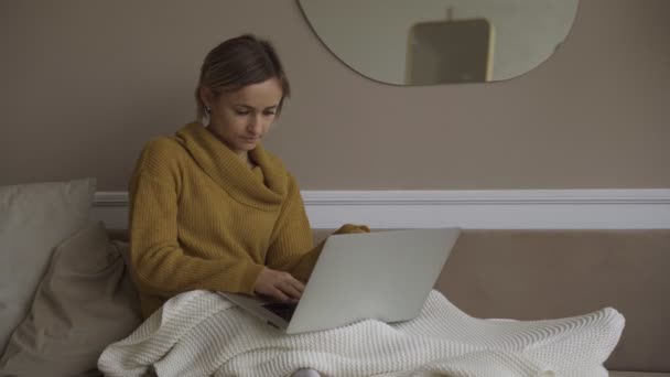 student using laptop at home lying on sofa under blanket using computer serching for online consultation. People and devices concept. - Кадри, відео
