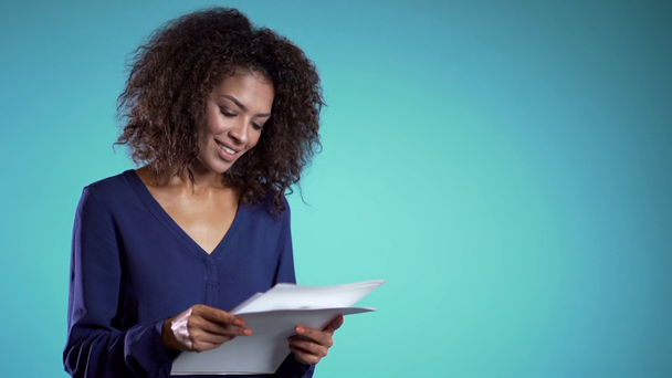 Copy space. Serious businesswoman standing on blue background. She is satisfied with work of staff. Pretty african american female boss checks documents, utility bills. - Filmati, video