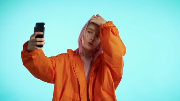 Girl with pink hair and extraordinary appearance make selfie on blue background. Using modern technology - smartphone, social networks - Materiał filmowy, wideo