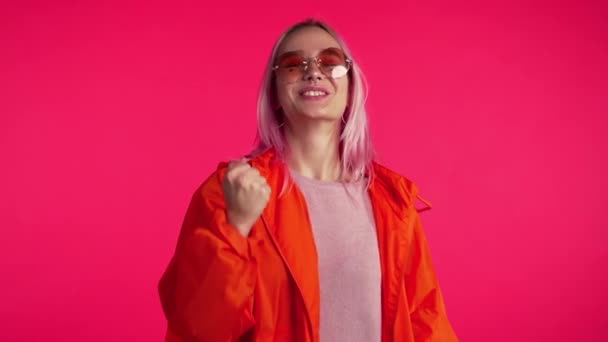 Girl with pink hair and extraordinary appearance shows yes gesture of victory,she achieved result, goals. Surprised excited happy hipster on red background - Video