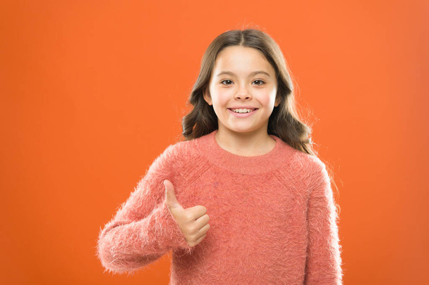 Secret of Success. carefree childhood. her healthy smile. happy childrens day. cute little girl smiling. small kid autumn sweater. feel success of style. cheerful child thumb up orange background - 写真・画像