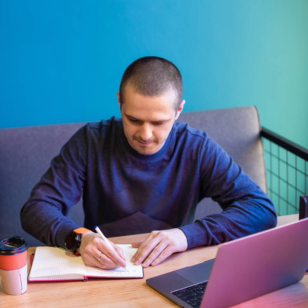 Чоловік з ноутбуком щось пише в блокноті
 - Фото, зображення