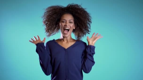 Surprised excited happy african woman jumping with ecstatic face expressions. Winning young female model on blue background. - Footage, Video