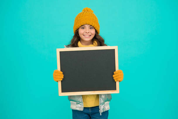 Presentation concept. Smiling girl wear winter outfit blank chalkboard copy space. Fresh information. Information for children. Happy holidays. Show information. Winter entertainment and activities - Foto, afbeelding