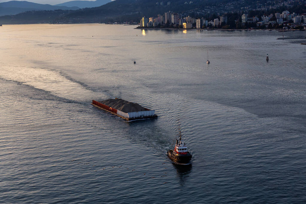 West Vancouver, British Columbia, Canada. Aerial View of a Tugboat in a modern cityscape on the Pacific Ocean Coast during an Autumn sunny and cloudy sunset. - Valokuva, kuva