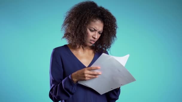 Serious african businesswoman boss on blue background. She is unsatisfied with work of staff. Young female office employee checks documents, reports. - Footage, Video