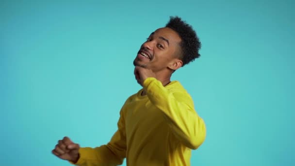 African man in yellow dancing on blue studio background. Positive smiling guy portrays happiness, harmony, fun. Slow motion. - Felvétel, videó
