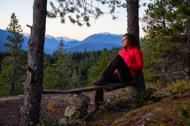 Adventurous Girl relaxing on a bench in the mountains during a sunny Autumn Sunset. Taken Squamish, North of Vancouver, British Columbia, Canada. Concept: Adventure, freedom, lifestyle - Foto, imagen