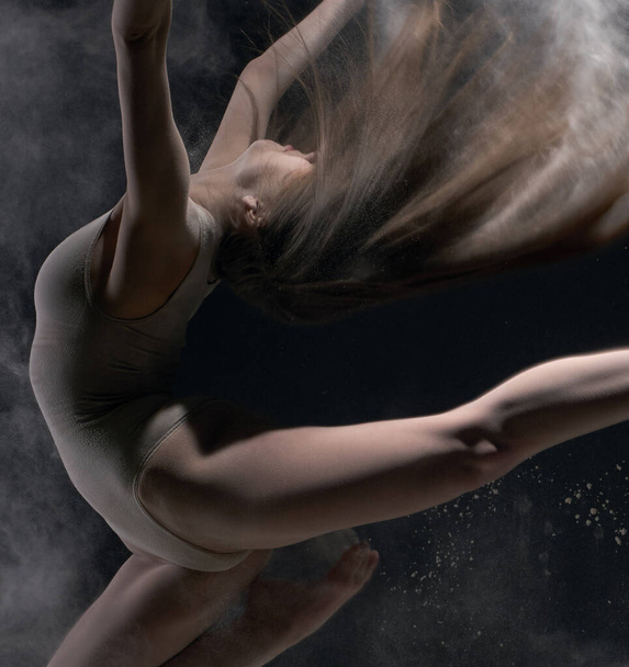 Girl in body jumps in dust cloud black background - Foto, imagen