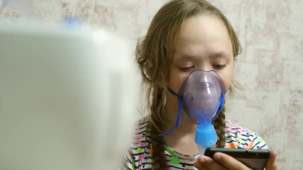 Nemocná dívka v masce vdechne lahvičku se sprejem a hraje počítačovou hru na tabletu. Dítě v modré nemocniční masce vdechuje výpary z dýchacích cest do plic. Léčba kašle. Detailní záběr - Záběry, video