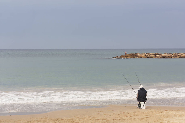Zeegezicht met een eenzame visser die met zijn rug naar de kijker zit - Foto, afbeelding