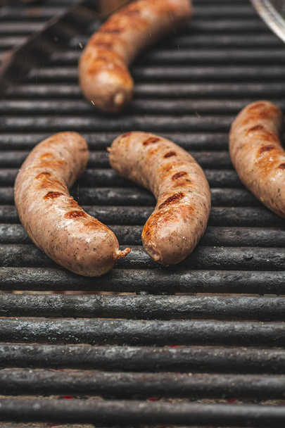 Sizzling juices jumping off savory brats cooking on an outdoor iron grill. - Fotografie, Obrázek