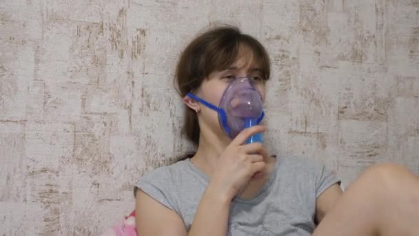 Una ragazza malata viene inalata da un nebulizzatore seduto su un divano. La donna con la maschera. Inspirare vapori per le vie respiratorie nei polmoni. Trattamento della tosse
 - Filmati, video
