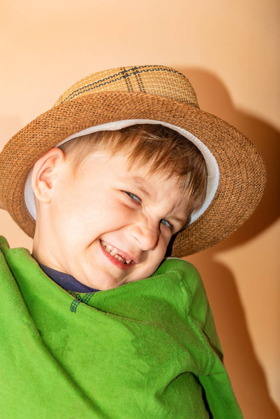 Menino alegre e feliz em um chapéu de palha e roupas verdes sorrindo e olhando para a câmera
. - Foto, Imagem