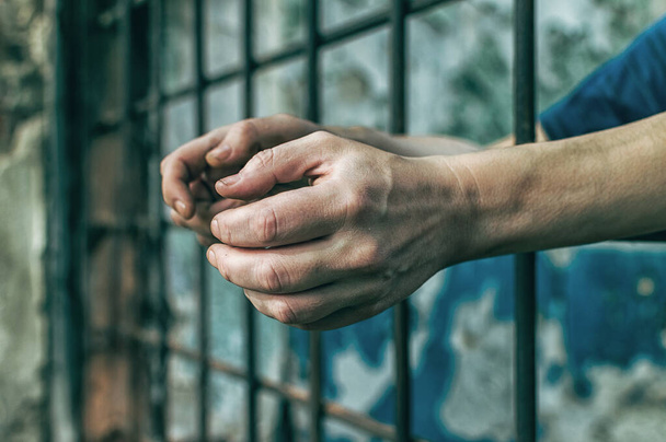 A depressed man holds his hands on the prison bars. Prisoner for the crime. Poor conditions. Scream, despair, pain, hunger. - Fotoğraf, Görsel