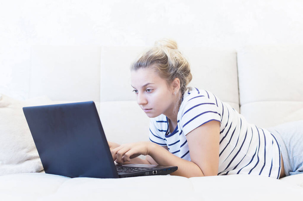 blonde girl is sitting at home on the couch with a laptop and communicates on the Internet. social networks. dating. - Foto, afbeelding