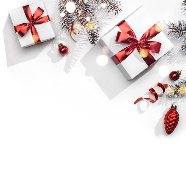 Весёлая рождественская открытка из еловых ветвей, подарочных коробок, красного декора, блеска и конфетти на белом фоне. Рождество и Новый год, боке, свет. Плоский, вид сверху - Фото, изображение