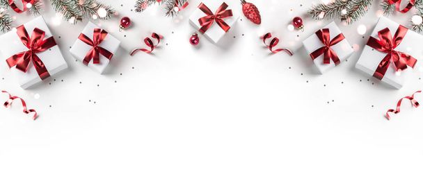 白い背景にモミの枝、ギフトボックス、赤の装飾、輝きとコンフェッティで作られたメリークリスマスカード。クリスマスと新年の休日、ボケ、光。フラットレイアウト、トップビュー - 写真・画像