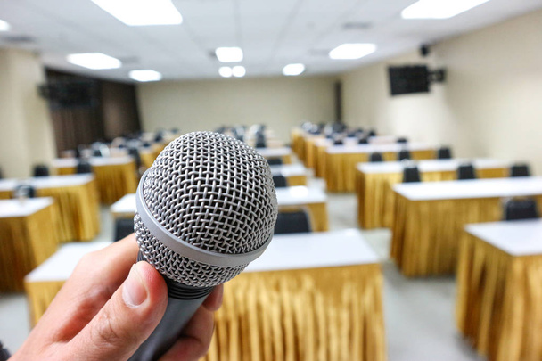 Ανθρώπινο χέρι κρατώντας ένα μικρόφωνο για να προετοιμαστεί για ομιλία ή τραγούδι στην τάξη. - Φωτογραφία, εικόνα