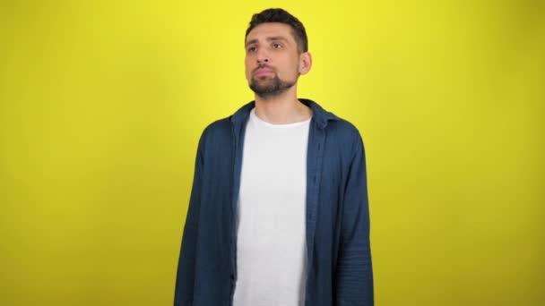A young man in a blue shirt and white T-shirt sneezes and covers his mouth with his hands. Yellow background. 4k slowmotion footage - Footage, Video
