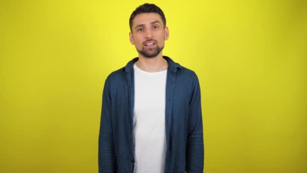 Ein junger Mann in blauem Hemd und weißem T-Shirt blickt in die Kamera, nickt und bejaht. gelber Hintergrund mit Kopierraum. 4k Zeitlupe - Filmmaterial, Video