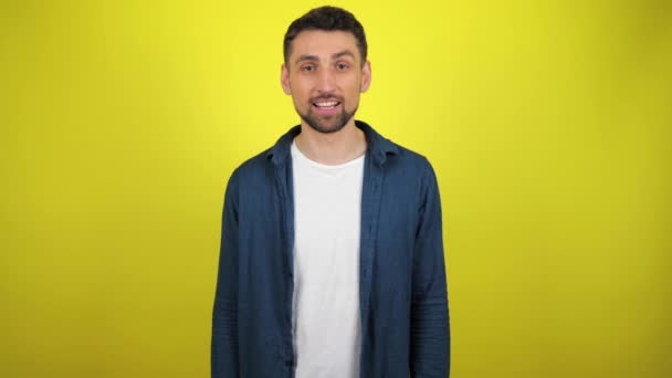 A young man in a blue shirt and white T-shirt is looking to the camera, nods his head and says yes. Yellow background with copy space. 4k slowmotion footage - Footage, Video