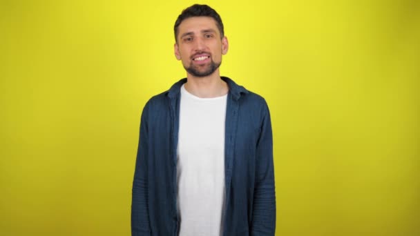 A young man in a blue shirt and white T-shirt is looking to the camera, nods his head and says yes. Yellow background with copy space. 4k slowmotion footage - Footage, Video
