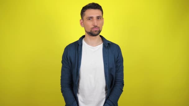 Ein junger Mann in blauem Hemd und weißem T-Shirt blickt in die Kamera, dreht den Kopf und sagt nein. gelber Hintergrund mit Kopierraum. 4k Zeitlupe - Filmmaterial, Video