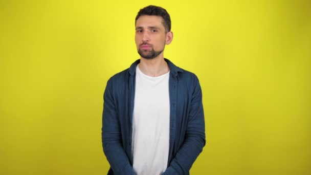 Mladý muž v modré košili a bílém tričku se dívá do kamery, otočí hlavu a řekne ne. Žluté pozadí s kopírovacím prostorem. Snímek zpomalení 4k - Záběry, video