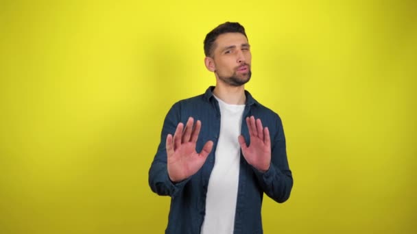 A young man in a blue shirt and white T-shirt is strictly gesturing with hands shape meaning denial saying NO. Yellow background with copy space. 4k slowmotion footage - Footage, Video