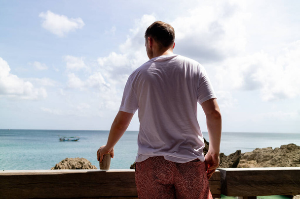 Mężczyzna pijący na wakacjach patrząc w morze - Zdjęcie, obraz