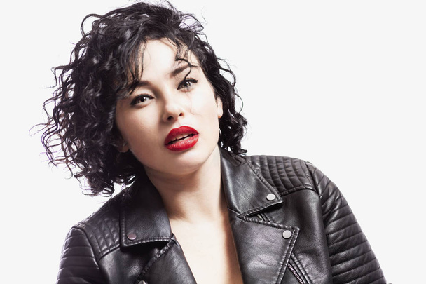 Young sexy woman in a leather jacket. Bright curly brunette with red lips. Close-up. White background. - Foto, Imagen