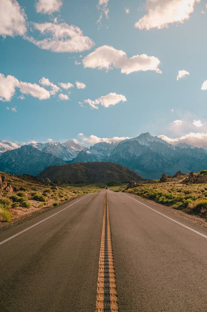 A vertical shot of a road with the magnificent mountains under the blue sky captured in California - 写真・画像