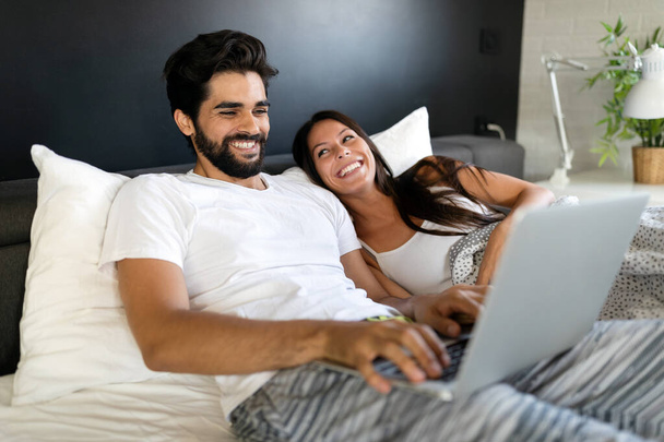 Young happy couple with laptop in the bed in room - 写真・画像