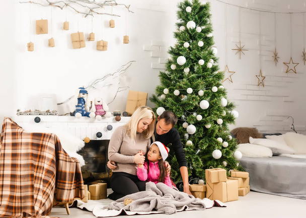 Neujahr. Weihnachten. Familie. junge Eltern und ihre kleine Tochter verbringen Zeit zusammen am heimischen Weihnachtsbaum - Foto, Bild