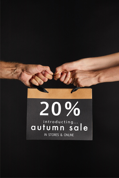 partial view of woman and man holding paper shopping bag with 20 percent autumn sale illustration isolated on black, black Friday concept - Zdjęcie, obraz