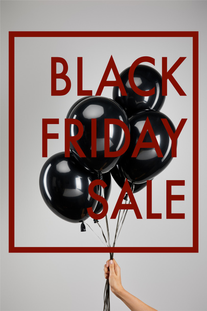 partial view of woman holding bunch of black balloons isolated on grey with black Friday sale illustration - Valokuva, kuva