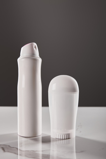 enrollar y rociar botellas de desodorante sobre una mesa de mármol aislada en gris
 - Foto, imagen