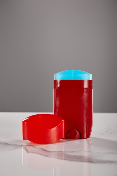 κόκκινο ρολό σε μπουκάλι αποσμητικό σε μαρμάρινο τραπέζι απομονωμένο σε γκρι - Φωτογραφία, εικόνα