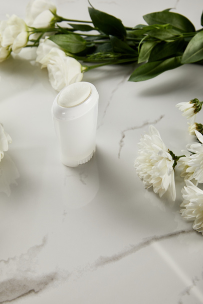 Beyaz mermer yüzeyde çiçekli deodorant şişesi üzerine seçici odaklanma - Fotoğraf, Görsel
