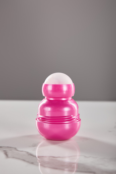 Pembe deodorant şişesinde yuvarlan mermer masada gri renkte izole edilmiş. - Fotoğraf, Görsel