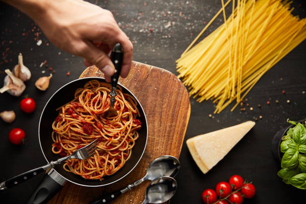bijgesneden beeld van de mens zetten vork in smakelijke bolognese pasta in koekenpan op zwarte achtergrond - Foto, afbeelding