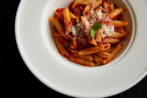 top view of tasty bolognese pasta with tomato sauce and Parmesan in white plate isolated on black - Photo, Image