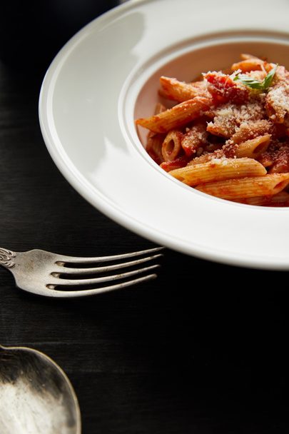tasty bolognese pasta with tomato sauce and Parmesan in white plate near cutlery on black wooden background - Photo, Image